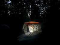 Tent in the woods, lantern light from within